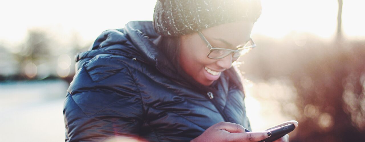 smiling woman wearing black coat using smartphone