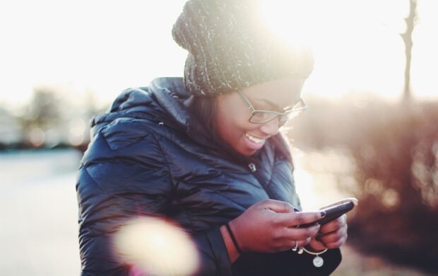 smiling woman wearing black coat using smartphone