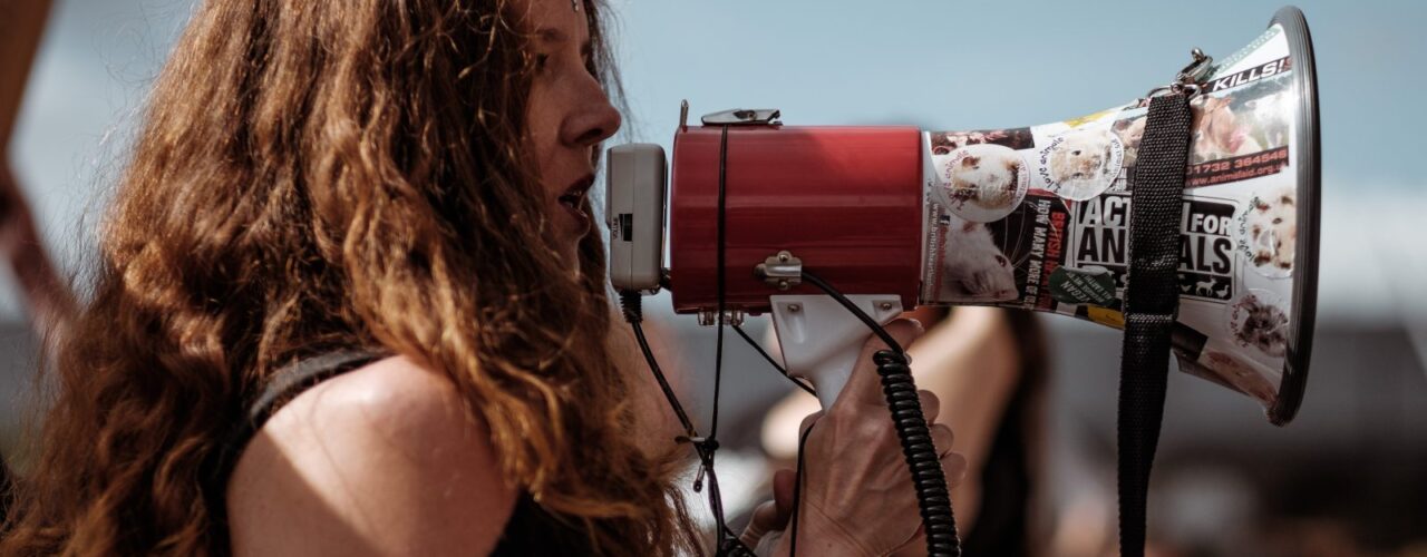 selective focus photography of woman wearing black cold-shoulder shirt using megaphone during daytime