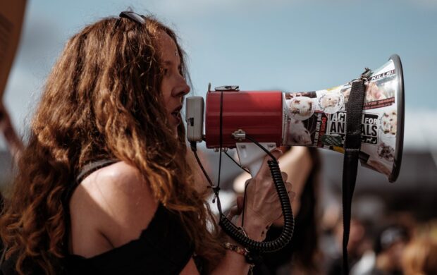 selective focus photography of woman wearing black cold-shoulder shirt using megaphone during daytime