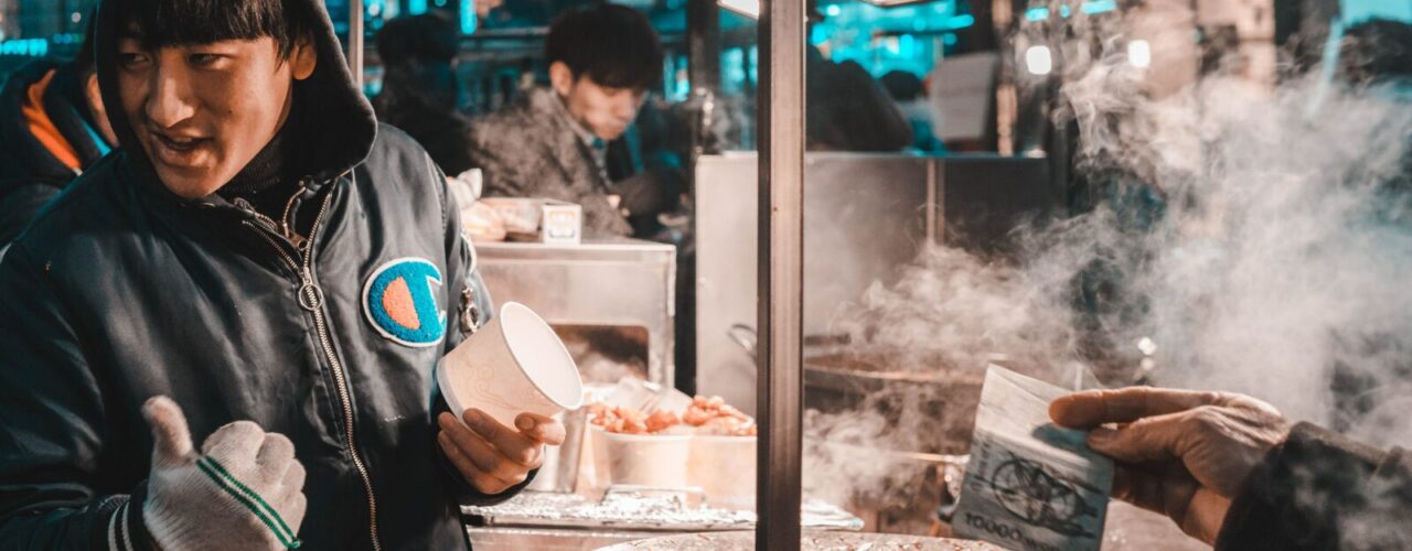 man holding disposable cup standing beside food cart