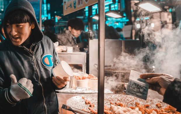 man holding disposable cup standing beside food cart