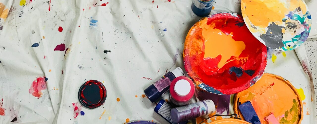 assorted-color paints and paintbrushes on white tarp