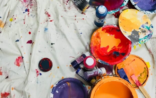 assorted-color paints and paintbrushes on white tarp