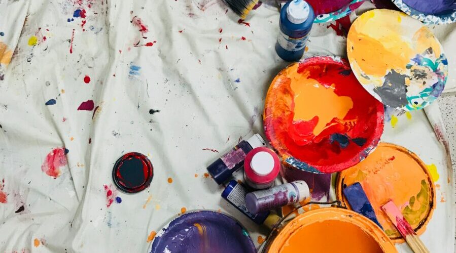 assorted-color paints and paintbrushes on white tarp