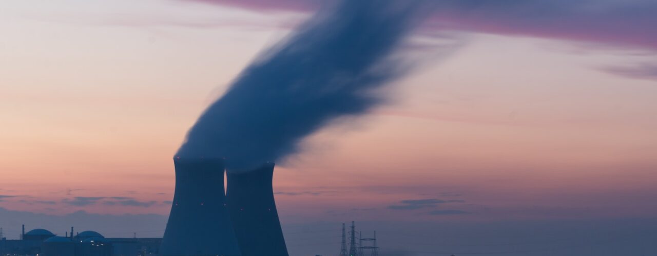 skyline photography of nuclear plant cooling tower blowing smokes under white and orange sky at daytime