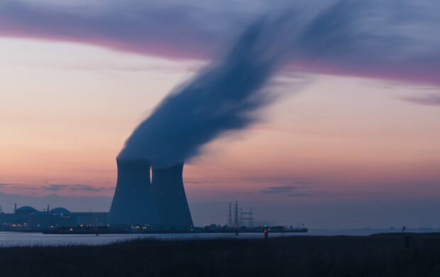 skyline photography of nuclear plant cooling tower blowing smokes under white and orange sky at daytime