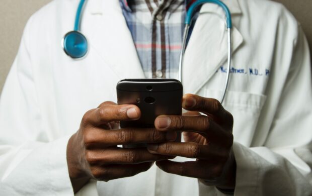 person wearing lavatory gown with green stethoscope on neck using phone while standing